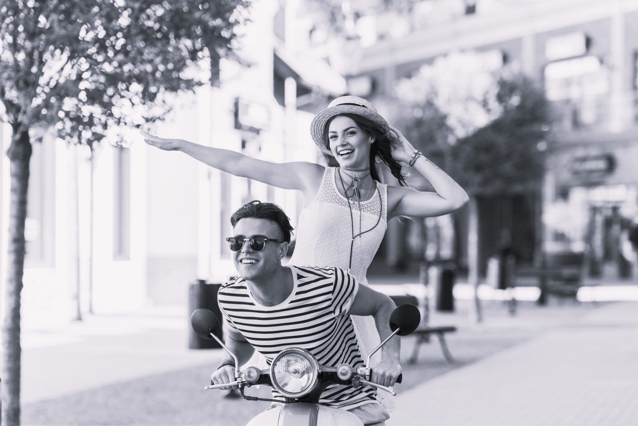 Handsome man in sunglasses and happy young woman in straw hat riding moped and smiling