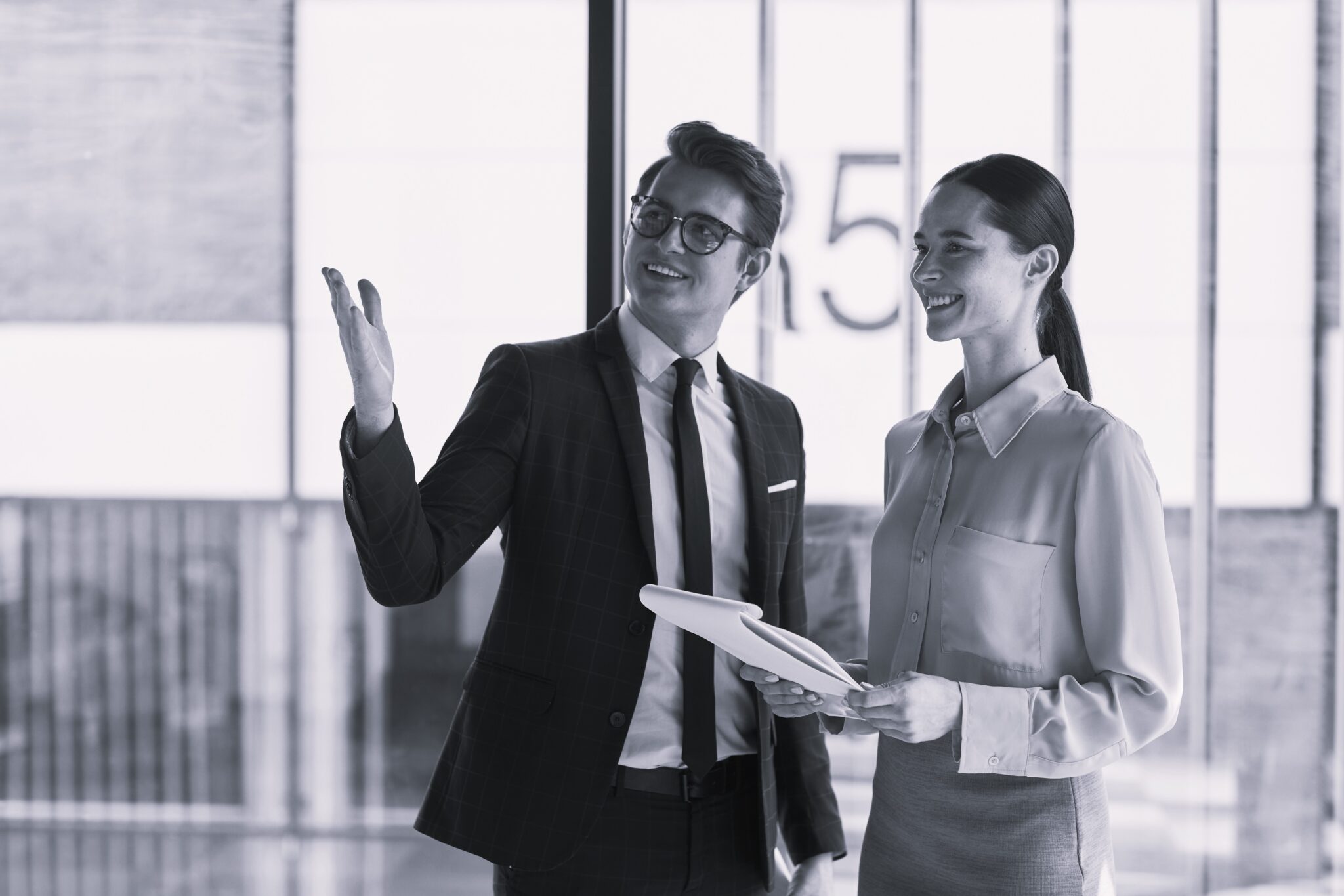 Waist up portrait of smiling real estate agent discussing property with female client and pointing up while standing in empty office building interior lit by sunlight, copy space